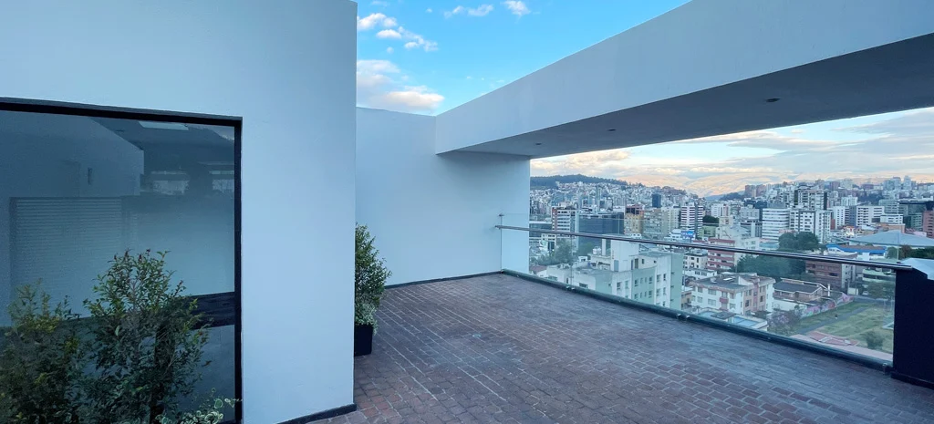 Fotografía de la terraza de Kamay al atardecer: piso de ladrillo, baranda de vidrio y vista a la ciudad.