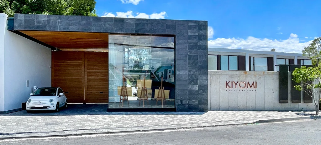Fotografía de la fachada de Kiyomi: revestimiento oscuro, ventanal de vidrio y letrero sobre muro de concreto.