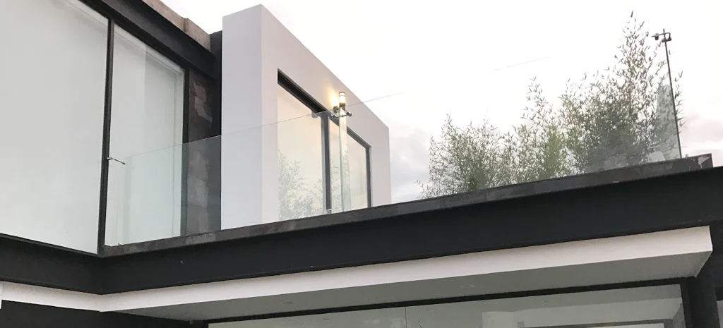 Fotografía de Domaine Cuatro: terraza con baranda de vidrio, muro blanco y volumen oscuro, con árboles y cielo nublado.