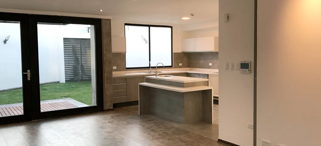 Fotografía de Domaine Cuatro: cocina abierta con isla gris, muebles claros y puertas de vidrio hacia un patio con césped.
