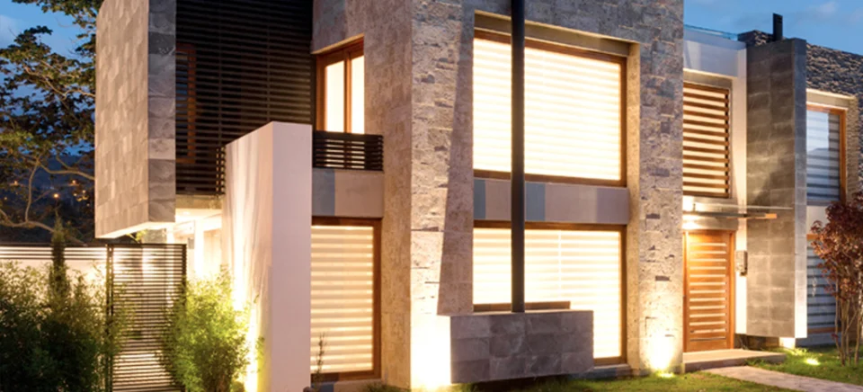 Fotografía de una casa de Domaine III al anochecer: fachadas de piedra, celosías de madera y ventanas iluminadas.