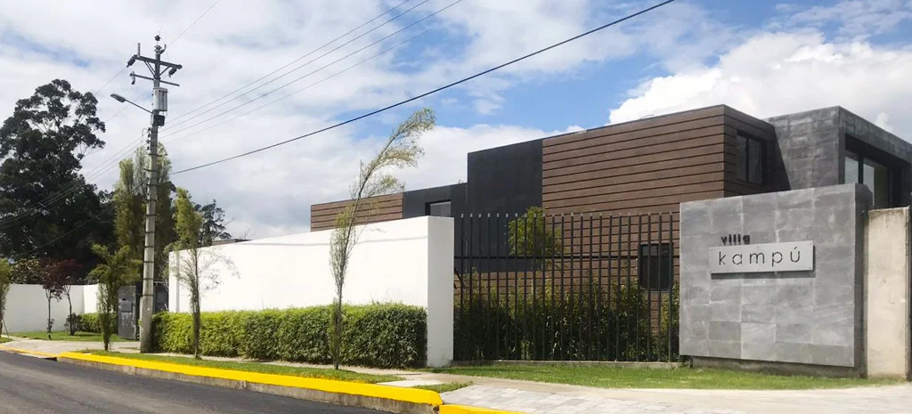 Fotografía de la entrada de Villa Kampú: muro blanco, letrero de piedra con el nombre y fachada de madera oscura.