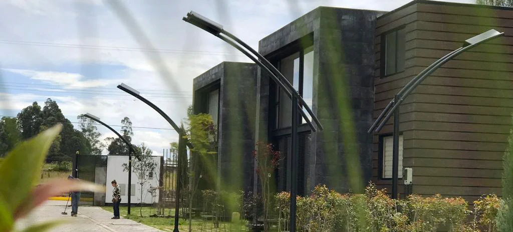 Fotografía de Villa Kampú: postes de luz curvos frente a casas de piedra oscura y madera, con una persona en la acera.