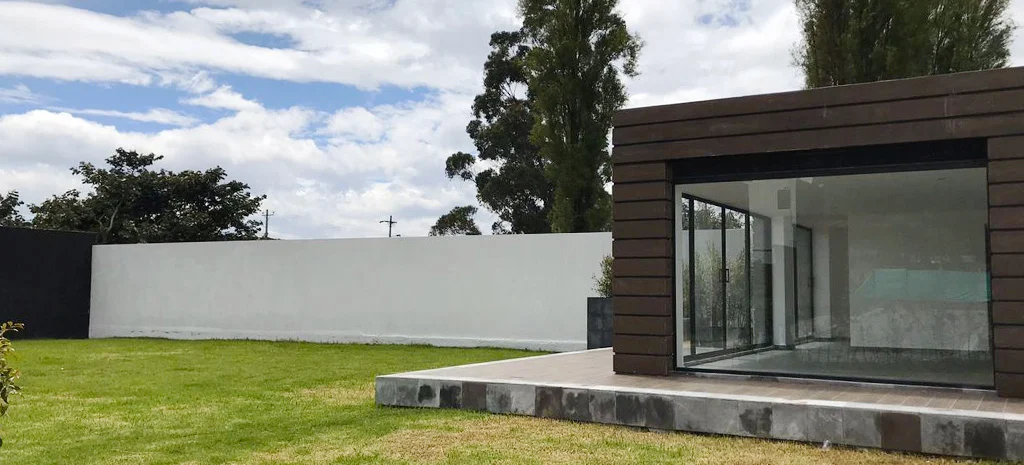 Fotografía del acceso de Villa Kampú: portón metálico negro, muro de piedra oscura y letrero con el nombre.