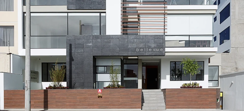 Fotografía de la fachada de Bellevue: revestimiento oscuro con su nombre, vidrio, muros de tono madera y escalinata.