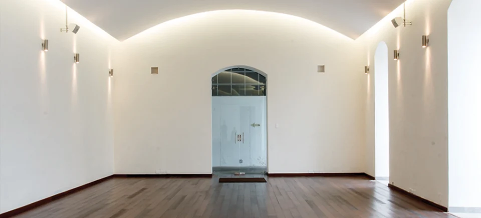 Fotografía del interior del Convento San Agustín: sala vacía de techo abovedado, paredes blancas, apliques y piso de madera.