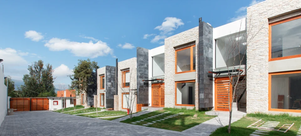 Fotografía de Domaine: fila de casas con revestimiento de piedra, marcos de madera, patio pavimentado y árboles, de día.