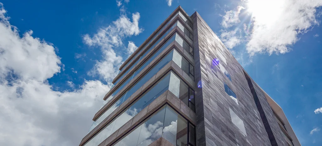Fotografía de la torre de Kamay tomada desde abajo: fachada de paneles oscuros, balcones de vidrio y cielo con nubes.
