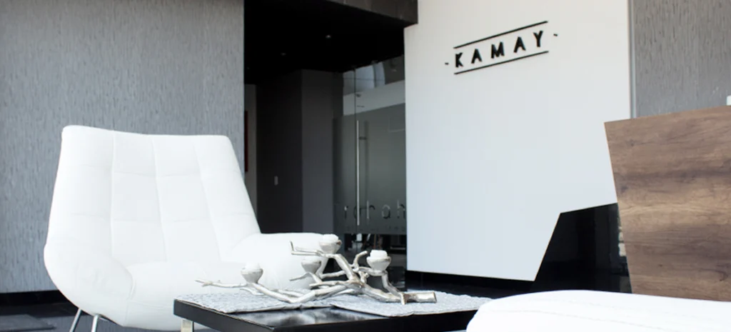 Fotografía de Kamay: sillón blanco tapizado, centro de mesa metálico y letrero KAMAY sobre pared blanca.