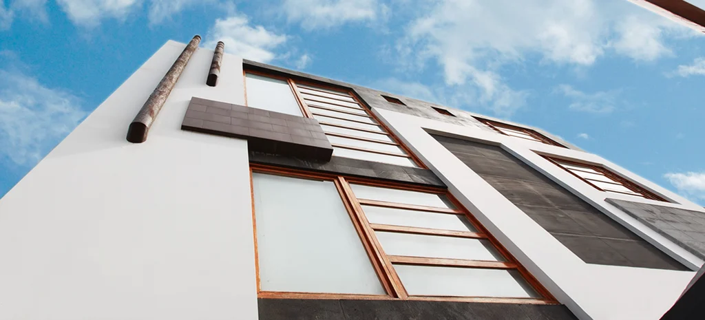 Fotografía del Edificio Monteserrín desde abajo: fachada con volumen blanco, paneles oscuros y ventanas con marco de madera.