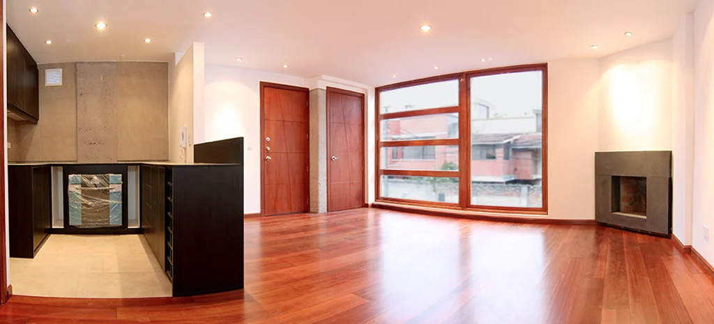 Fotografía del interior del Edificio Monteserrín: sala con piso de madera, ventanal con marco de madera y chimenea empotrada.