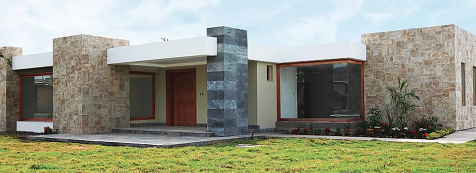 Fotografía de la fachada de Residencia Privada: casa de un piso con muros de piedra, puerta de madera y ventanal.